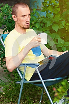 Man at backyard drinking coffee and reading book