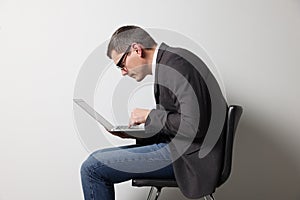 Man with bad posture using laptop while sitting on chair against grey background