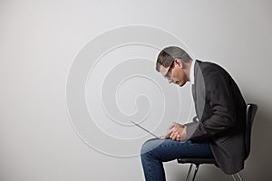 Man with bad posture using laptop while sitting on chair against grey background. Space for text