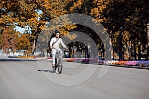 Man with bag on bike, smiling at camera on background of park, outdoors