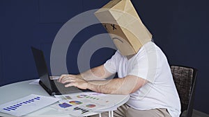 A man with a bag on his head with a drawn sad emoticon works