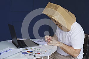 A man with a bag on his head with a drawn sad emoticon works