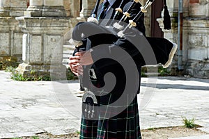A man with a bagpipe, a kilt in a cage with a green and red stripe. Culture. The details of the skirt of the kilt and