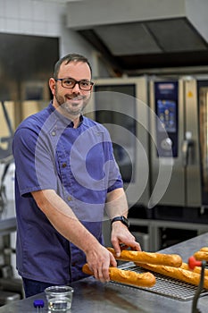 Man baker baking baguettes in bakehouse photo