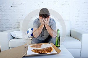 Man with ball pizza and beer bottle watching football game on tv covering eyes sad and disappointed for failure or defeat
