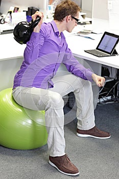 Man on ball working out with kettlebell during offce work