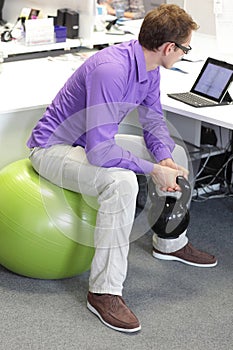 Man on ball working out with kettlebell during offce work