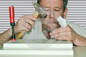 A man with a bandaged finger hammers a nail into the boards connected by a clamp