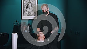 Man barber in black mask washing his client hair in barbershop