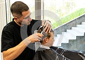 Man barber cutting little boy's hair using comb and scissors. Child getting haircut from adult male, likely barber