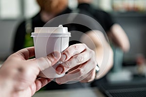 man barista hands gives paper coffee cup