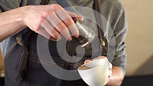 Man barista poured into a cup of coffee cinnamon in a modern coffee shop.