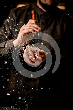 man bartender holds piece of ice and crushes it with trident and fragments fly around