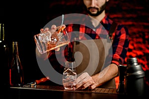 Man bartender professionally pours cocktail from mixing cup into small glass. photo