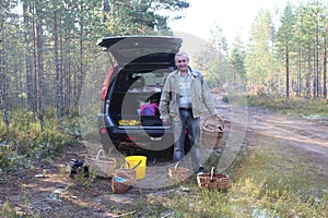 Man with a basket of cepes mushrooms in the forest and a car on background