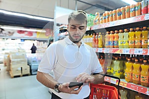 A man with a basket looks at the phone while shopping at a supermarket. Shopping in the store.