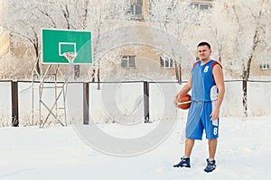 A man basketball player in blue sports uniform stands on a basketball court and holds a basketball in his hands in winter