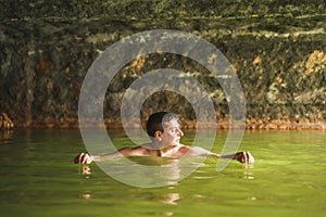 Man bathe swim in outdoor cave, dirty hot springs. Thermal water bath pool. Healthy natural clay. Yellow green mud. Spa