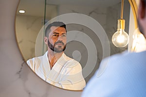 man in bathrobe looking at himself in the mirror.