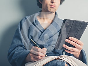 Man in bathrobe using tablet and taking notes