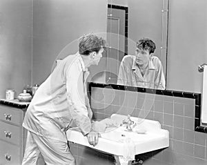 Man in bathroom looking into mirror photo