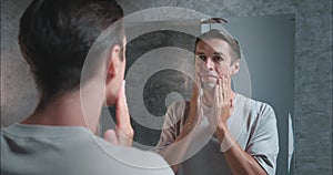 Man in bathroom looking at mirror applies moisturiser for face importance moisturise face for skin health. Moisturize