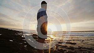 Man on the beach looking at beautiful sunset. Male watching far away at horizon and thinking. Enjoying the seascape.