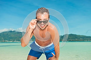 Man on the beach posing in briefs while fixing sunglasses