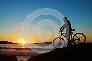 Man, beach and silhouette with mountain bike, sunset and mockup space by waves for summer cycling adventure. Cyclist