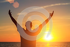 A man on the beach at sunset shows his hands how happy he is with the concept of travel and relaxation