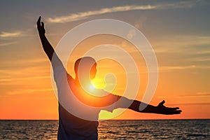 A man on the beach at sunset shows his hands how happy he is with the concept of travel and relaxation