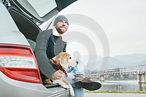 Man with beagle dog siting together in car trunk. Late autumn ti