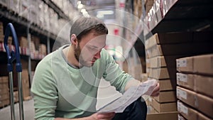 A man with a beard in a blue sweater checking his list in a warehouse