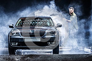 A man with a beard or car washer washes a gray car with a high-pressure washer at night in a shop wash