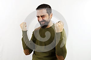 A man with beard and casual clothes, very happy and excited doing the winner gesture with closed fists and arms raised, smiling an