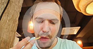 A man with a beard eating noodles with chopsticks in a diner