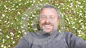 Man with beard enjoys spring in green meadow background Guy taking selfie photo on smiling face lying on grass