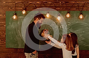 Man with beard in formal suit teaches schoolgirls physics. Teacher and girls pupils in classroom near chalkboard