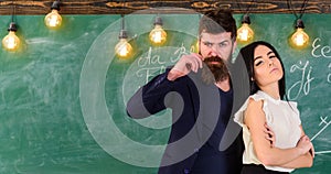 Man with beard and girl teacher stand in classroom, chalkboard on background. Partners concept. Teacher and strict
