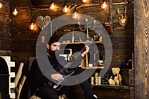 Man with beard holds black electric guitar. Man bearded musician enjoy evening with bass guitar, wooden background. Guy