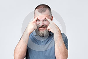 Man with beard holds fingers on temples, trying to remember something.