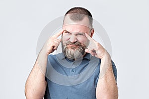 Man with beard holds fingers on temples, trying to remember something.