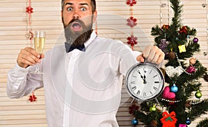 Man with beard holds glass of champagne and alarm clock