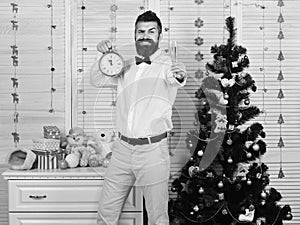 Man with beard holds glass of champagne and alarm clock