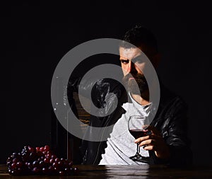 Man with beard holds glass of wine on dark brown background. Sommelier tastes expensive drink. Winetasting and