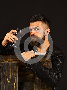 Man with beard holds glass of wine on dark brown background. Winetasting and degustation concept. Sommelier tastes photo