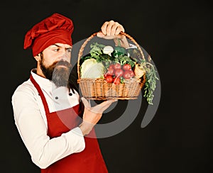 Man with beard holds veggies on black background.