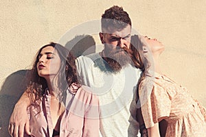 Man with beard hugs two ladies on hot sunny day. Threesome suffers of heat on summer day, wall on background. Girls