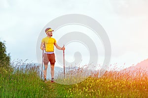 Man with beard looks away while walking on the path in the middle of mountain meadows with stick