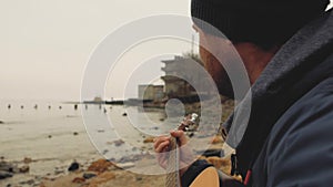 A man with a beard makes a photo of the sea on cameraa guy with a beard and a hat playing a guitar near the sea